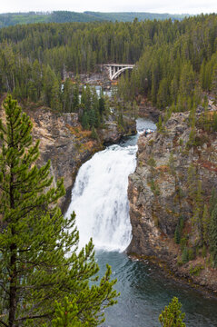 Waterfall cascading down rocky cliffs in a forested mountainous landscape. Montana, USA