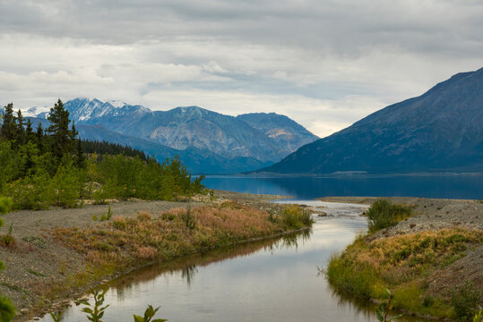 Serene mountain landscape with river, lush greenery, and cloudy sky reflections.   Yukon Territory, Canada