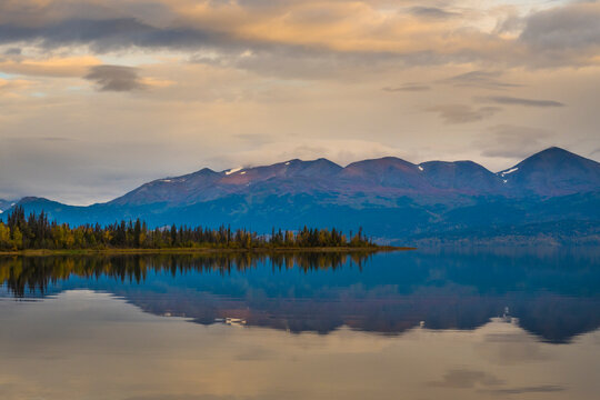 Tranquil lake reflecting mountains and clouds during a serene sunset with colorful sky. Skilak Lake, Alaska, USA