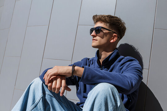 Young man in sunglasses sitting against a modern tiled wall in sunlight. Almeria, Spain