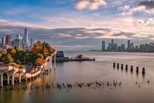 Scenic view of a bustling city skyline with a unique pier and calm waters at sunset. Little Island Park, New York City, USA