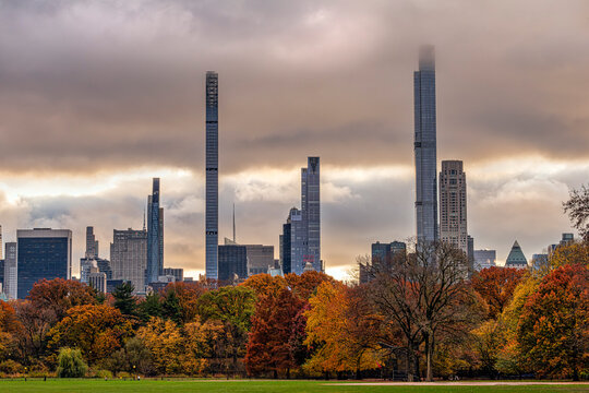 Central Park's colorful fall foliage with tall skyscrapers under a cloudy sky in the background. Central Park, New York City, USA