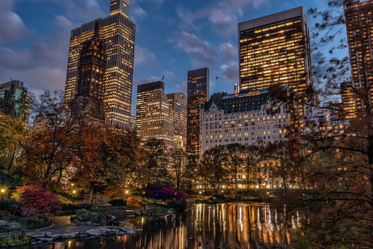 City skyline at dusk with reflections on a tranquil park pond and autumn foliage. Central Park Lake, New York City, USA