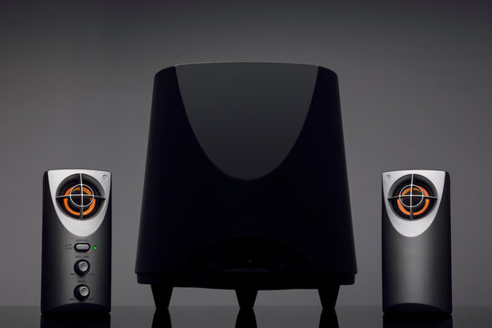 Black subwoofer with two compact speakers against a dark background.