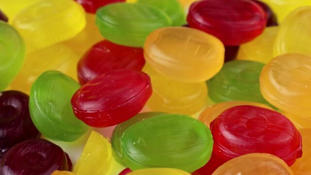 Glossy fruit-flavored hard candies in red, yellow, and green colors falling down close up
