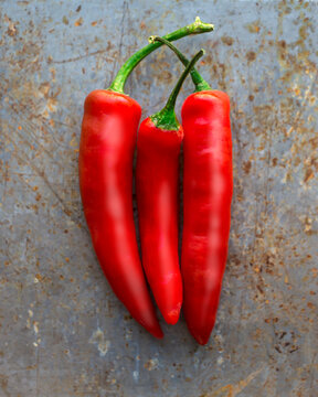 Three red chili peppers with green stems on a textured gray surface.