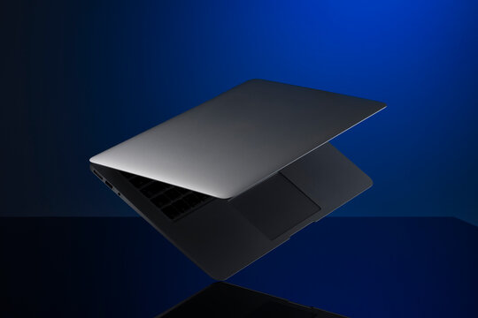 Sleek metallic laptop with partially closed lid against a deep blue background.
