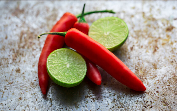 Fresh red chili peppers and halved green limes on a rustic metal surface.