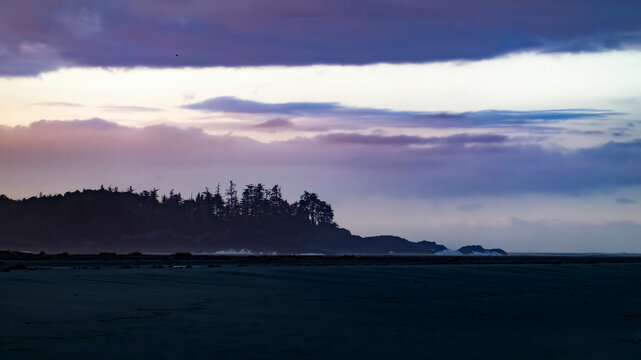 Dusk over a tranquil coastline with silhouetted trees against a colorful sky. Tofino, Vancouver Island, Canada