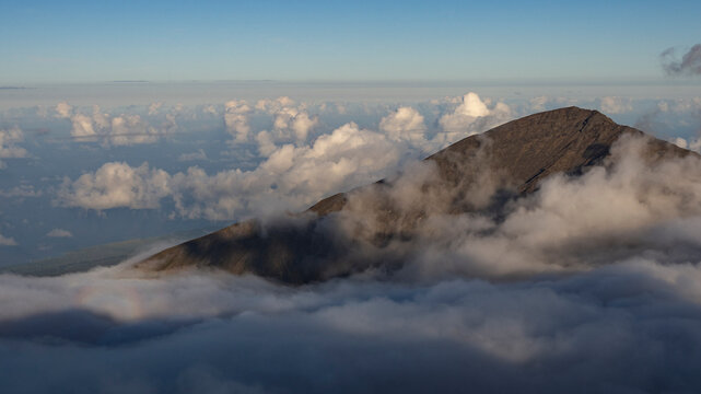 Mountain peak surrounded by fluffy clouds under a blue sky at sunrise. Kula, Maui, Hawaii, USA