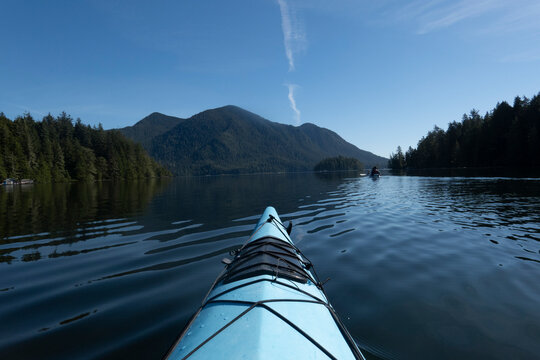 Blue kayak gliding on calm lake with mountains and clear blue sky in the background. Ucluelet, Vancouver Island, Canada