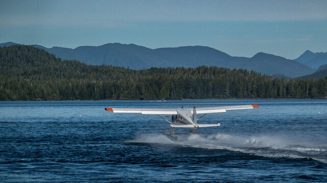 A seaplane taking off from a calm lake against a backdrop of forested mountains. Tofino, Vancouver Island, Canada