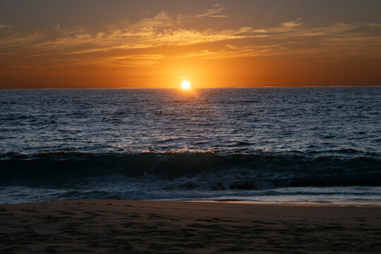 Golden sunset over ocean waves and sandy beach with a vibrant sky. Todos Santos, Baja California, Mexico