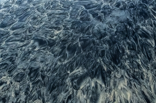 Abstract pattern of dark sand with flowing textures forming intricate designs on a beach. Todos Santos, Baja California, Mexico