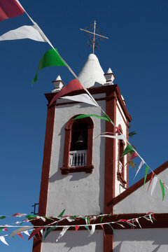 White church bell tower with red trim under a clear blue sky adorned with colorful flags. La Paz, Baja California Sur, Mexico