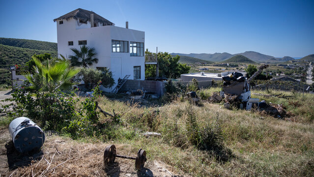 Abandoned house with damaged roof in a grassy field under clear blue sky. Todos Santos, Baja California, Mexico