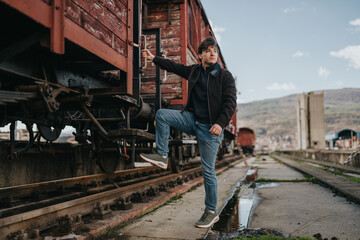 A young male tourist climbs onto a weathered vintage train car. The scene shows train travel at an old industrial railway platform.