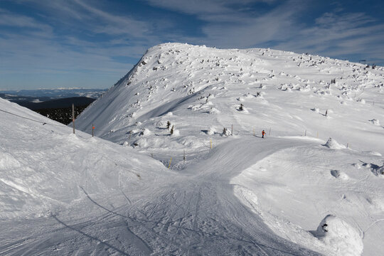 Snow-covered mountain landscape under a clear blue sky with one person skiing downhill. Kootenay Boundary, British Columbia, Canada