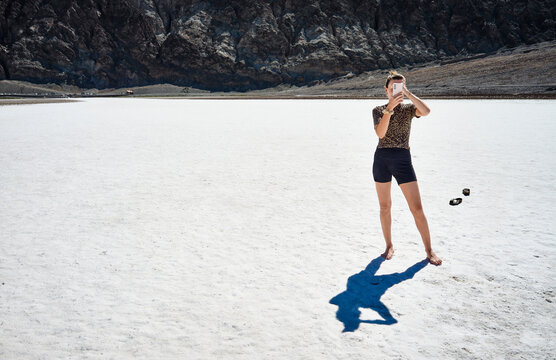 Person standing on a vast salt flat taking a photo with a mountain backdrop. Death Valley, California, USA