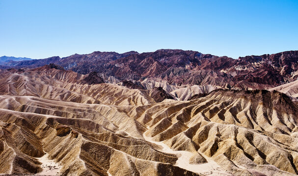 Rugged desert landscape with eroded hills under a clear blue sky. Death Valley, California, USA