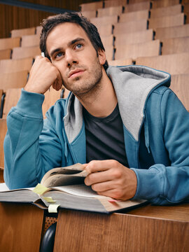 Young man in a lecture hall looking thoughtful while holding an open book. Germany