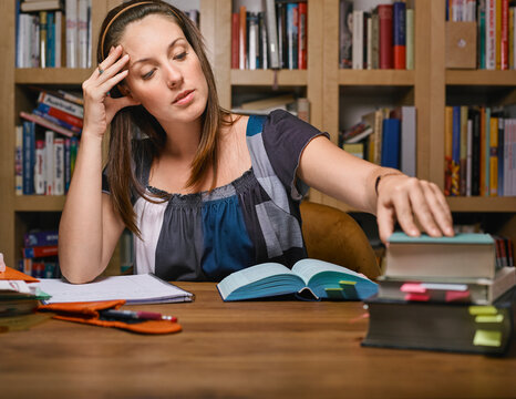 Woman studying at a wooden table with books and notes in a cozy library setting. Germany