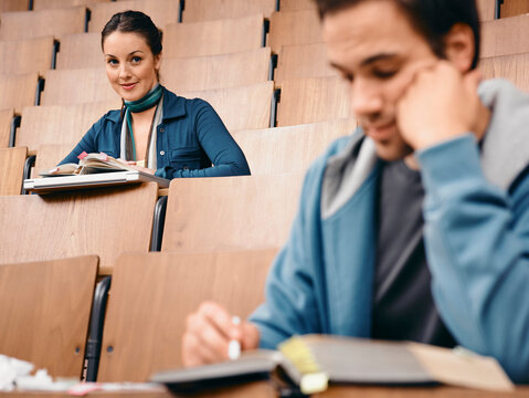 Woman in lecture hall looking at a man in front of her who is taking notes. Germany