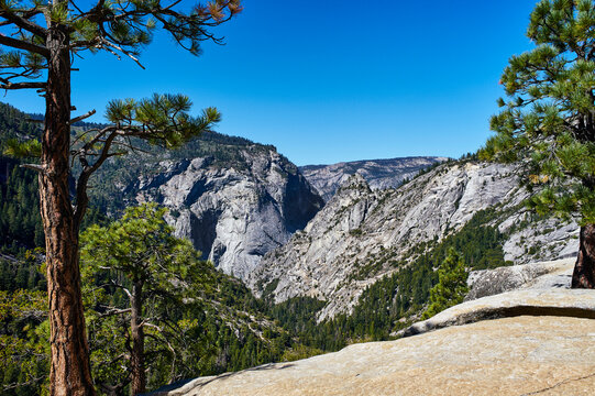 Majestic mountain landscape with rocky cliffs and lush pine trees under a clear blue sky. Yosemite National Park, California, USA