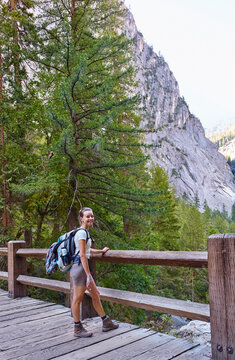 A female hiker with a large backpack stands on a wooden bridge in a forested mountain area. Yosemite National Park, California, USA
