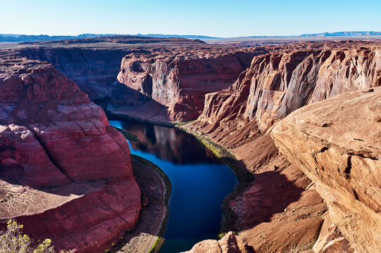 A winding river flows through a vast canyon under a clear blue sky with rugged orange cliffs. Horseshoe Bend, Colorado River, Arizona, USA