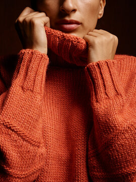 Close-up of a person in a cozy orange knit sweater with hands near face. Germany