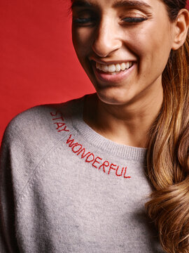 Smiling woman with long hair wearing a sweater with Stay Wonderful text on a red background. Germany