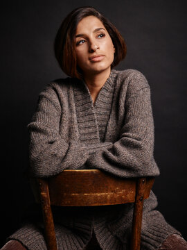 Woman in a cozy cashmere cardigan leans on a wooden chair against a dark background. Germany Germany
