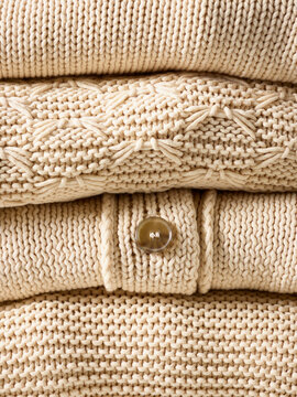 Neatly folded beige sweaters stacked, showcasing knitting patterns and a button detail. Germany