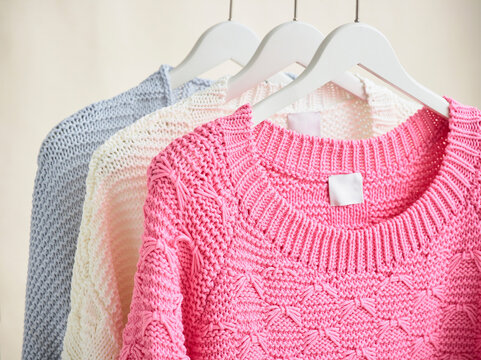 Three colorful knitted sweaters hang on white hangers against a neutral background.  Germany