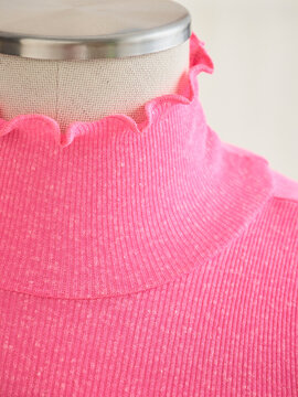 A mannequin showcases a bright pink ribbed turtleneck with a scalloped edge. Germany