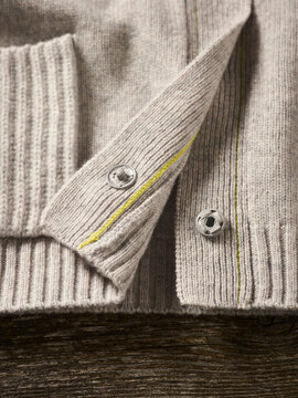 Close-up of beige knit sweater with metal snap buttons on wooden surface. Germany