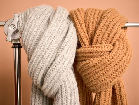 Close-up of two knitted scarves, grey and orange, draped over a silver metal rod. Germany
