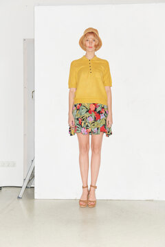 Woman in yellow blouse and floral skirt standing against a white background. Germany