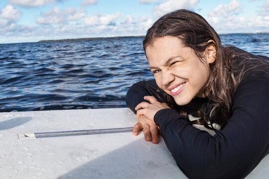 Smiling young girl on a boat, leaning on edge with ocean and blue sky in background. Baltic Sea, Germany