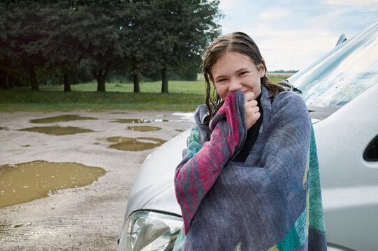 Young girl wrapped in a colorful towel smiling near a car on a rainy day. Baltic Sea, Germany
