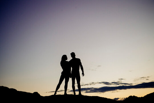 Silhouetted couple stands on a hilltop against a colorful sunset sky. WA, USA