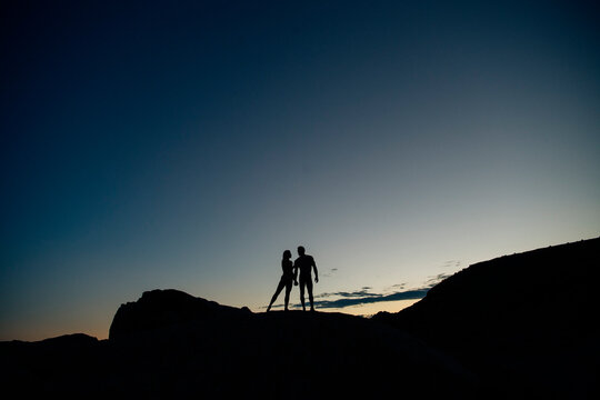 Silhouetted couple stands on a rocky hill against a gradient sunset sky. WA, USA