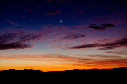 A stunning sunset with a crescent moon over silhouetted mountains and a vibrant sky gradient. WA, USA