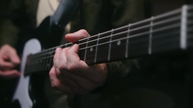 Close up view of a guitarist's hands playing chords and plucking strings on a black and white electric guitar during a studio session, showcasing musical skill and passion for rock music