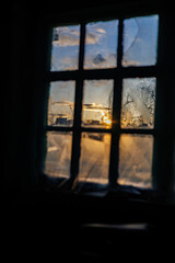 Fototapeta premium View of a golden sunset and snowy trees through an old rustic window: concept of nostalgia, winter coziness and solitude.