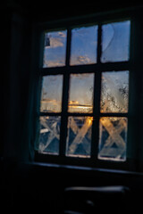 Fototapeta premium View of a golden sunset and snowy trees through an old rustic window: concept of nostalgia, winter coziness and solitude.