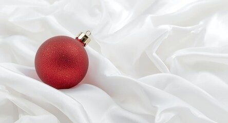 Fototapeta premium Christmas bauble resting on bright white smooth backdrop with copy space