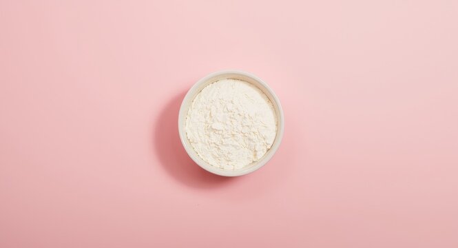 Bowl containing colostrum milk powder on smooth pink backdrop with ample room for text
