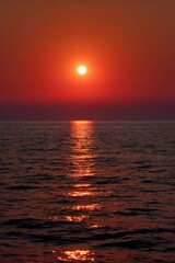 Fototapeta premium Intense red sunset over calm sea with bright sun reflection and smooth rippling water at dusk
